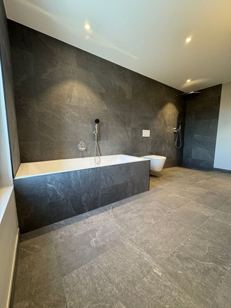 Salle de bain avec carrelage gris foncé effet pierre, baignoire et douche ouverte