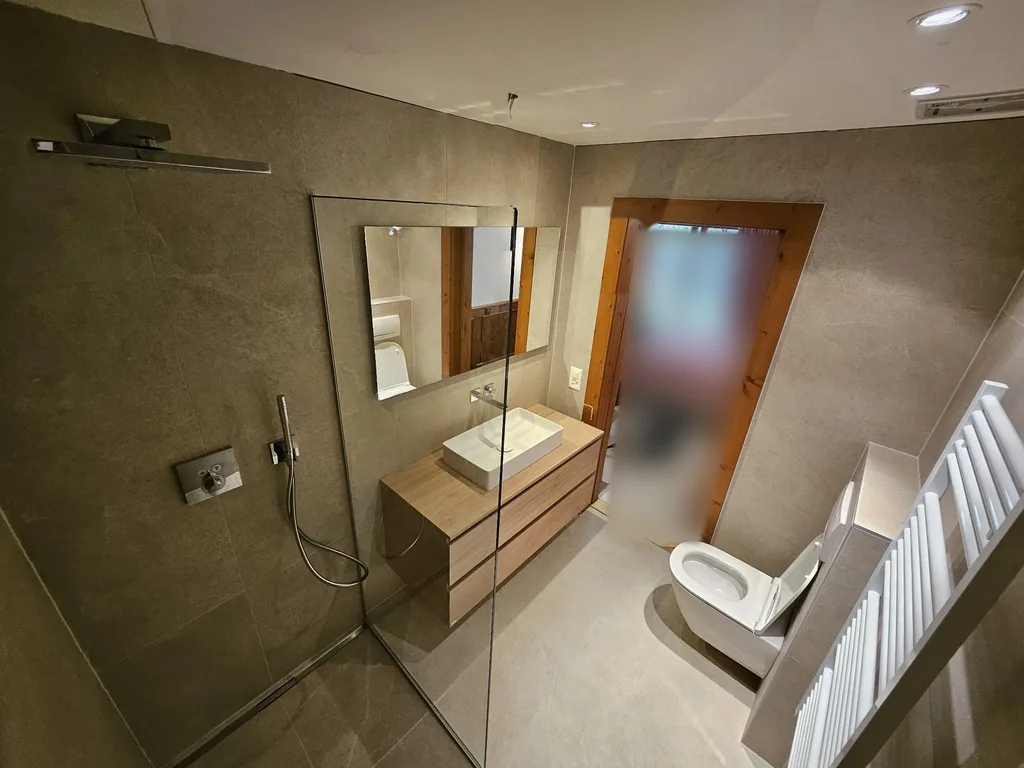 Salle de bain rénovée à Crans-Montana avec douche à l'italienne et meuble vasque en bois